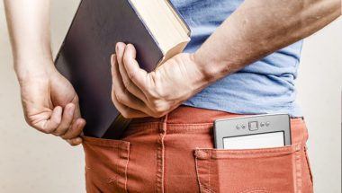 Man trying to cram large hardcover book in back pocket; his other pocket holds a better-fitting tablet