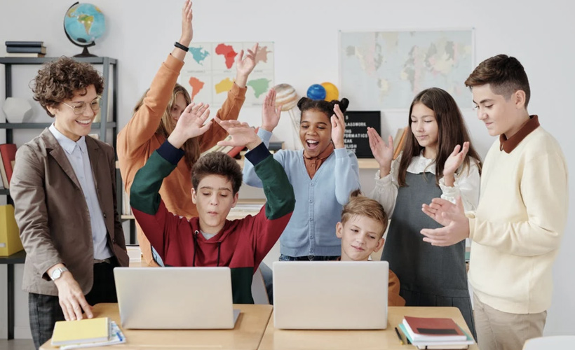 Happy students and teacher using multimedia in the classroom