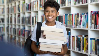 Boy with stack of books in arms at library