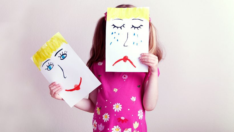 Girl with "happy face" and "sad face" pictures to help communication emotions