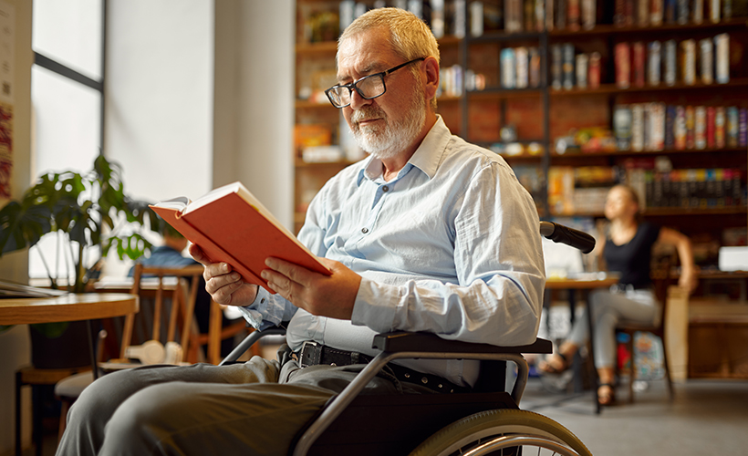 Older library patron in wheelchair reading a book