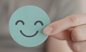 Fingers holding up a circular card with a happy face on it, representative of mental health