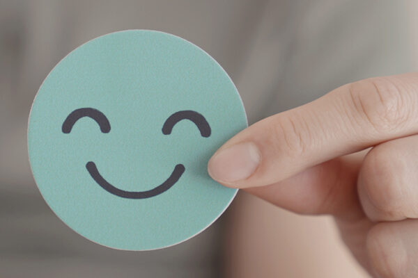 Fingers holding up a circular card with a happy face on it, representative of mental health