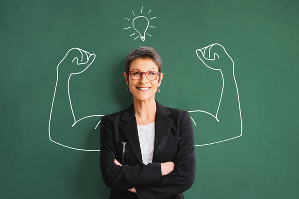 Empowered teacher standing against chalkboard with strong arms drawn on it