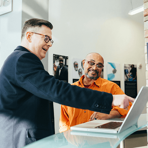2 man standing next to a laptop talking