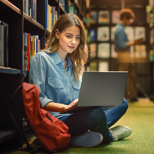 High school student sitting in the library looking at laptop